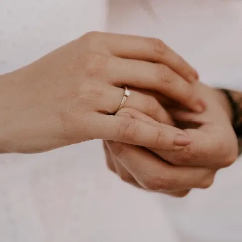 Nahaufnahme eines Verlobungsrings an der Hand einer Frau, gehalten von einer anderen Hand. Der Ring funkelt dezent und elegant.