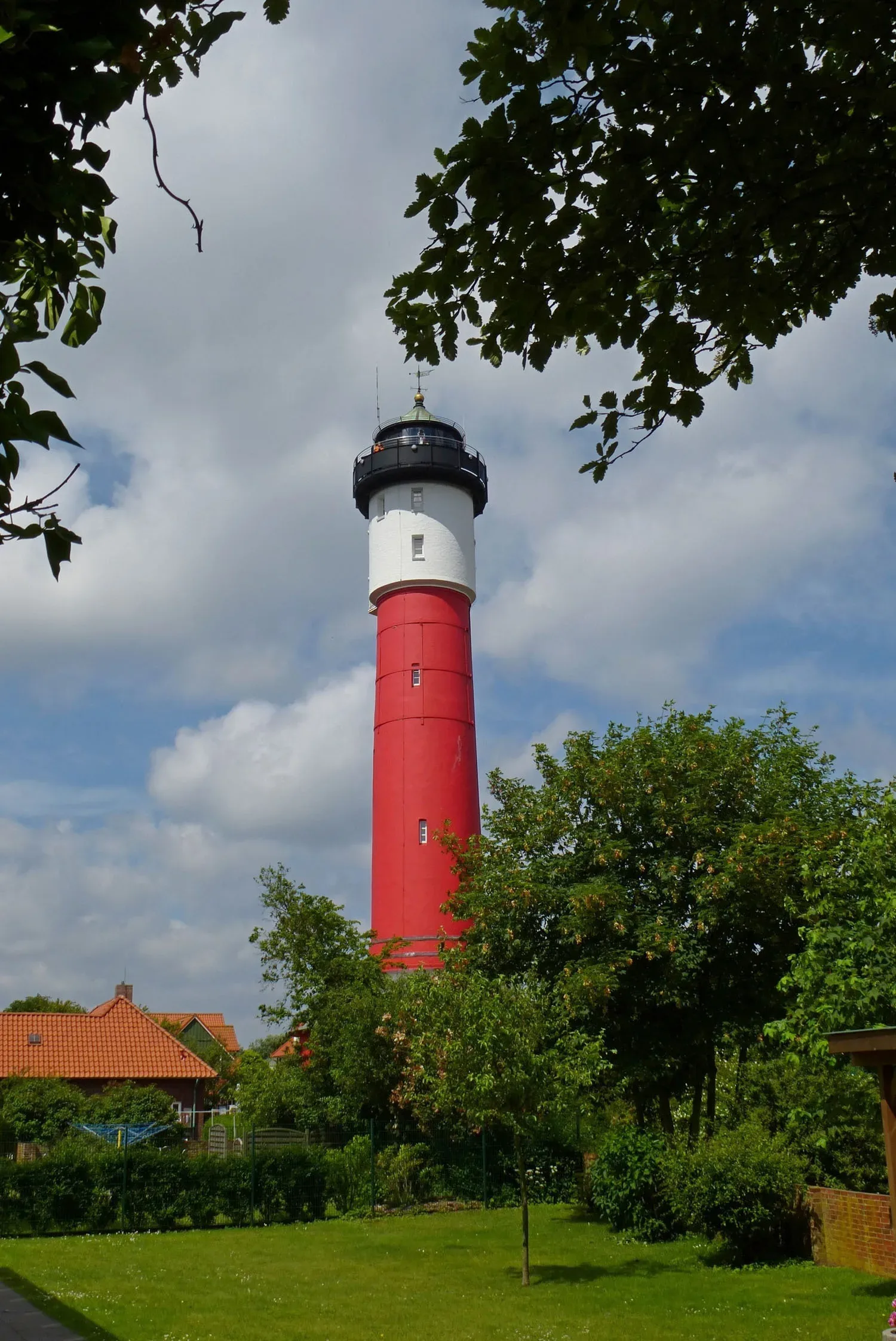 Der rot-weiße Leuchtturm auf Wangerooge erhebt sich imposant über die grüne Landschaft, umgeben von charmanten Häusern und Bäumen.