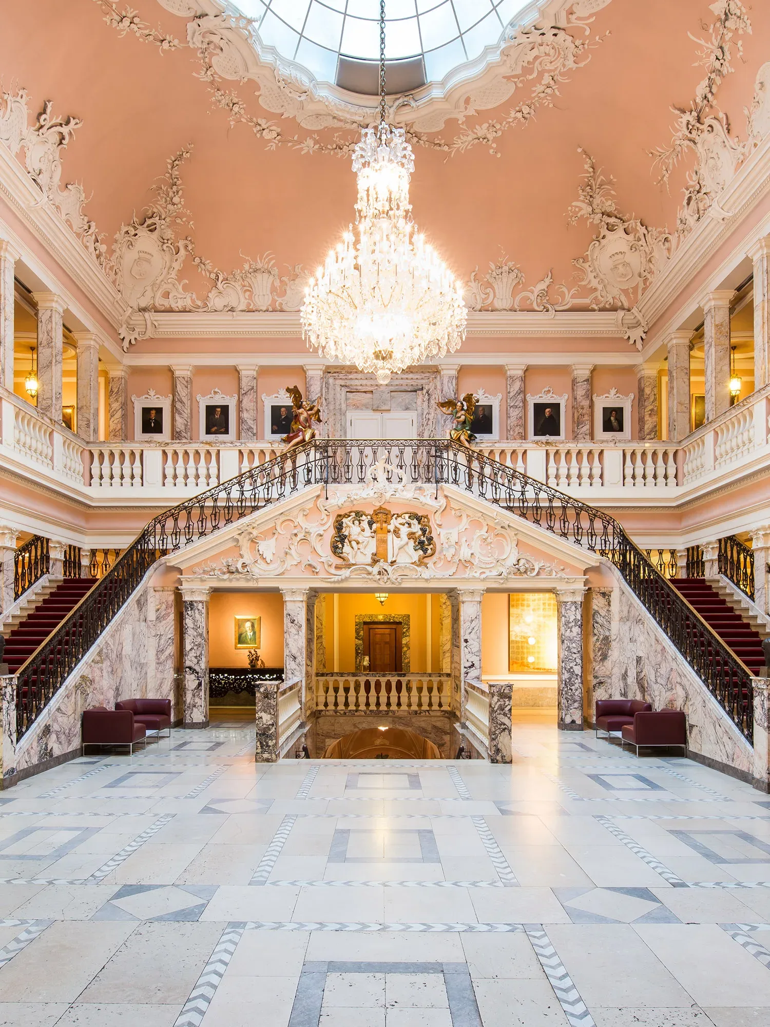 Elegantes Treppenhaus im Kurhaus mit opulentem Kronleuchter und aufwendigen Stuckarbeiten an der Decke.