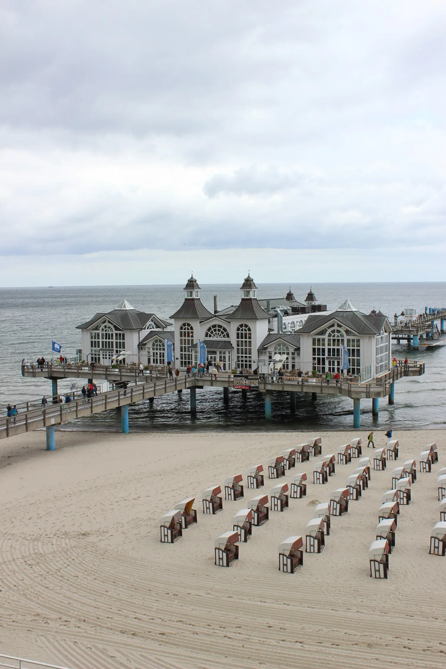 Die Seebrücke Sellin mit ihrem markanten, historischen Gebäude ragt in die Ostsee. Strandkörbe stehen ordentlich aufgereiht am Strand, während Besucher die Brücke entlanglaufen.
