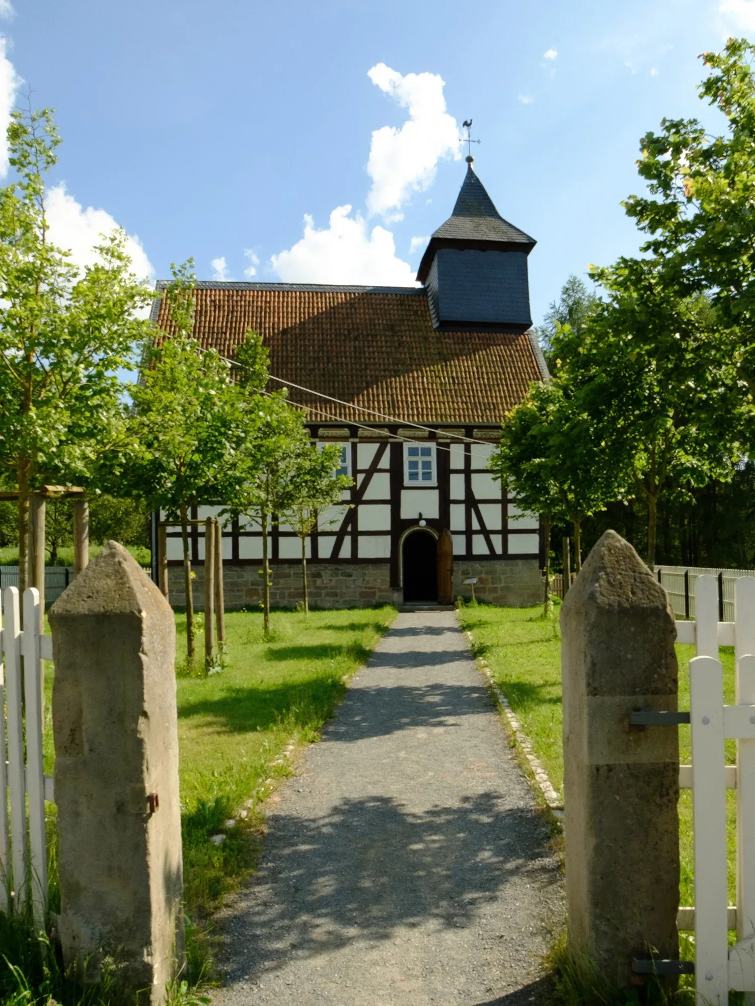 Die historische Fachwerkkirche im Freilichtmuseum Hessenpark, umgeben von Bäumen und einer ruhigen Gartenlandschaft.
