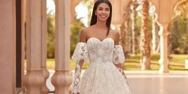 Braut in einem romantischen Spitzen-Ballkleid mit schulterfreien Puffärmeln und Herzausschnitt, in eleganter Außenkulisse.