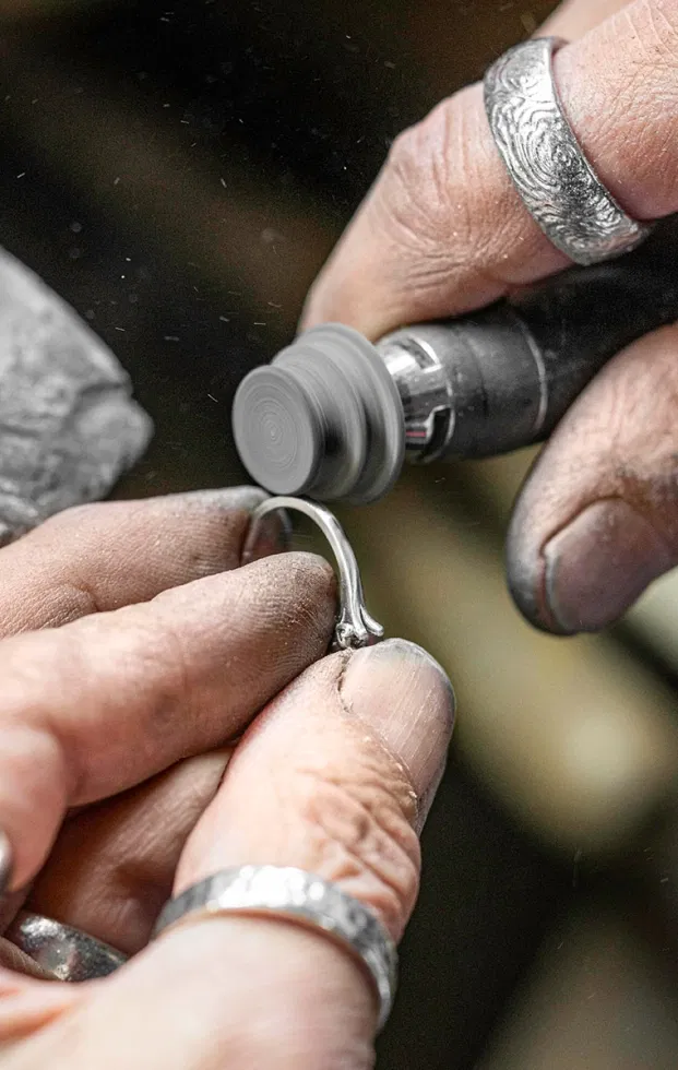 Detailaufnahme eines Juweliers beim Polieren eines Rings in der Manufaktur – handwerkliche Bearbeitung und Präzision im Fokus.