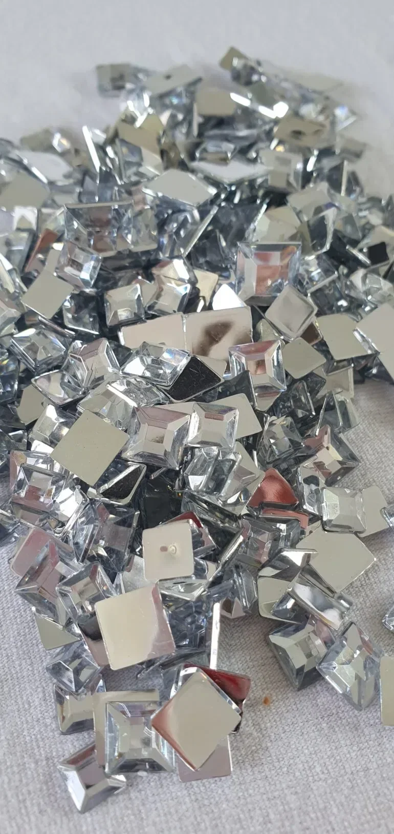 Nahaufnahme von silbernen Glitzersteinen in verschiedenen Formen, die für ein DIY-Projekt bereitliegen und funkelndes Licht reflektieren.