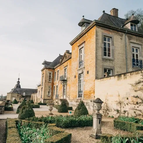 Historisches Herrenhaus aus Stein mit gepflegten Hecken und einem formalen Garten im Vordergrund, ideal für eine elegante Hochzeitslocation.