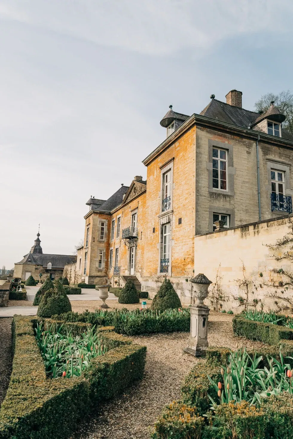 Historisches Herrenhaus aus Stein mit gepflegten Hecken und einem formalen Garten im Vordergrund, ideal für eine elegante Hochzeitslocation.
