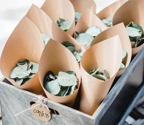 Eukalyptusblätter in kleinen Papierkegeln, arrangiert in einer Holzkiste, als stilvolle Alternative zu traditionellem Hochzeitskonfetti.