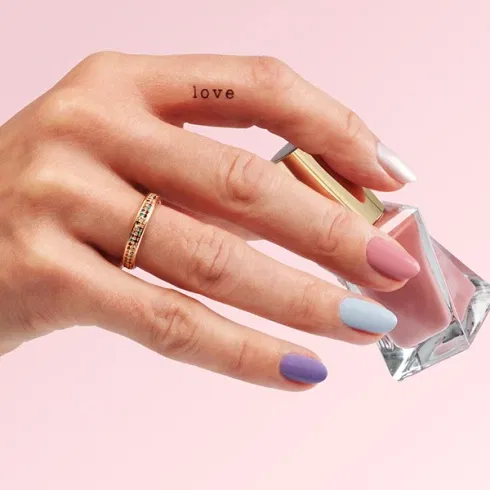 Nahaufnahme einer Hand mit pastellfarbenem Nagellack und Love-Tattoo – perfekte Hochzeitsinspiration.