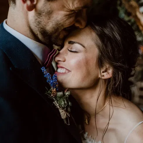 Glückliches Brautpaar in einem zärtlichen Moment, die Braut lächelt liebevoll und lehnt sich an den Bräutigam.