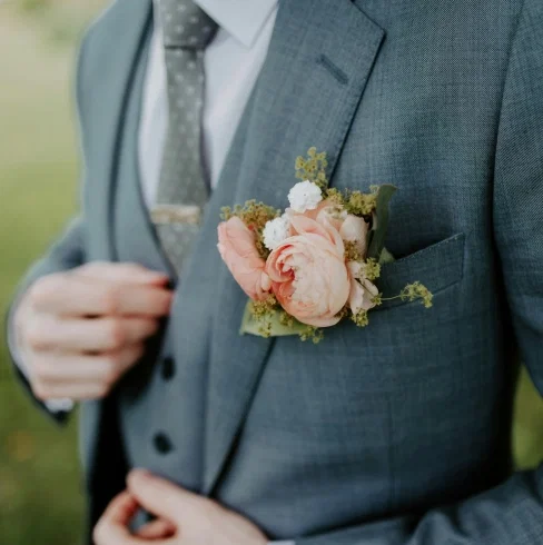 Detailaufnahme eines eleganten Hochzeitsanzugs mit grauer Krawatte und floraler Ansteckblume aus Rosen und kleinen Blüten in sanften Pastellfarben.