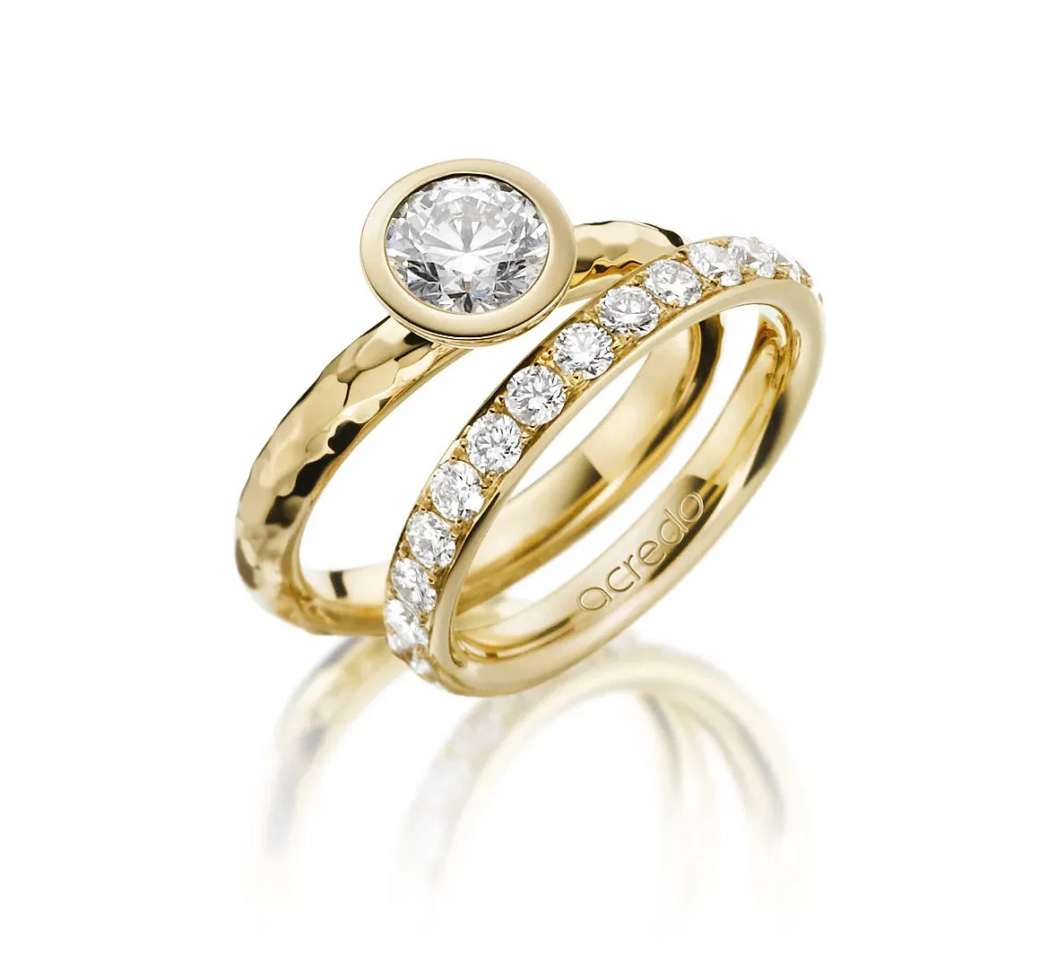 Zwei elegante Gelbgoldringe, einer mit einem großen Diamanten in einer Zargenfassung und der andere mit einem Band aus kleineren Diamanten besetzt. Der Kontrast zwischen dem gehämmerten und glatten Gold verleiht den Ringen einen besonderen Charme.