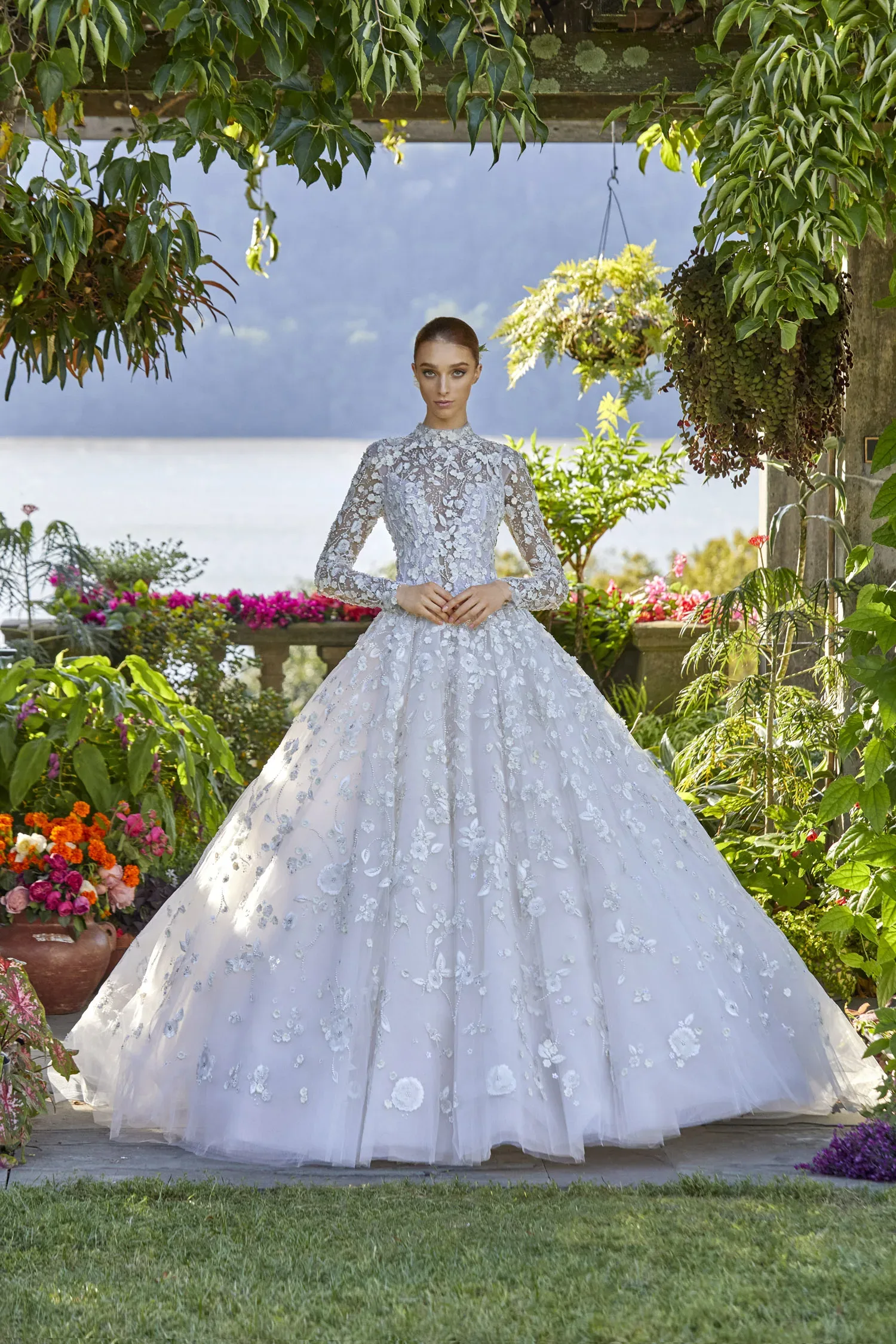 Elegantes Brautkleid mit hochgeschlossenem Spitzenoberteil und floralen Details, getragen von einem Model in einem blühenden Garten.