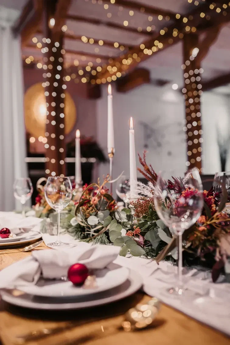 Festlich gedeckter Tisch mit Kerzen und weihnachtlicher Blumendekoration. Die warmen Lichterketten und eleganten Gedecke schaffen eine festliche Atmosphäre.