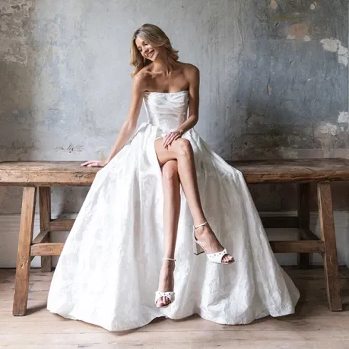 Braut in einem klassischen weißen Kleid sitzt stilvoll auf einem rustikalen Holztisch.