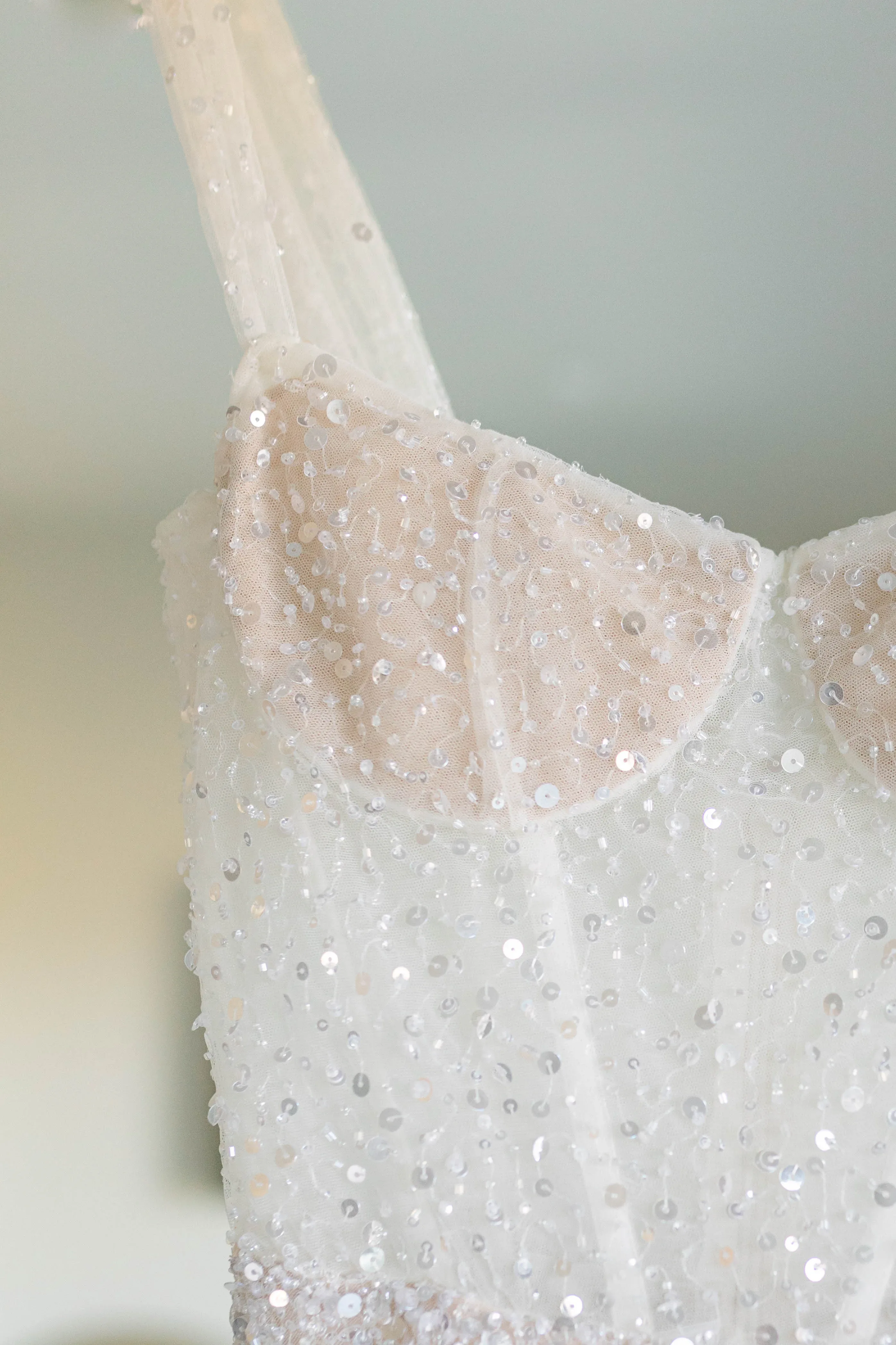 Nahaufnahme eines glitzernden Brautkleids mit funkelnden Pailletten und zarten Trägern, das elegant an einem Bügel hängt.