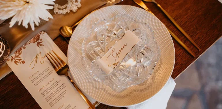 Elegante Hochzeitstischdekoration mit Kristallgeschirr, goldenen Bestecken und einer Menükarte, stilvoll arrangiert für den Bräutigam.