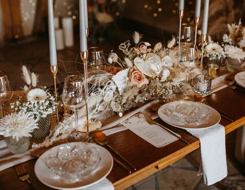 Elegant gedeckte Hochzeitstafel mit Kristallgeschirr, goldenen Bestecken und einem Blumengesteck in Pastellfarben, umgeben von hohen Kerzenleuchtern.