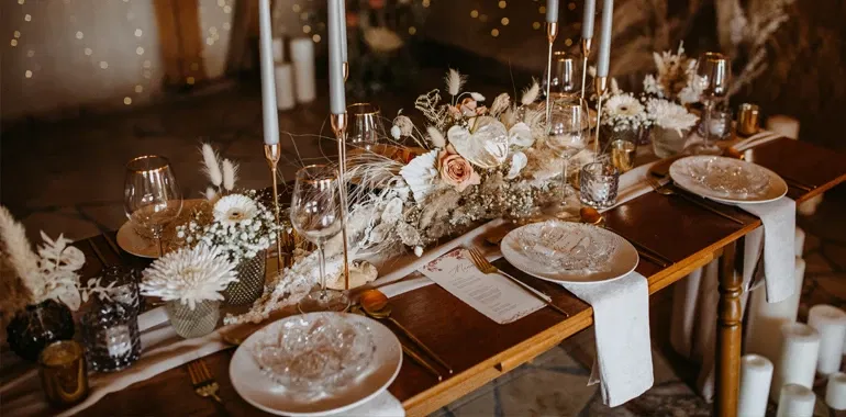 Elegant gedeckte Hochzeitstafel mit Kristallgeschirr, goldenen Bestecken und einem Blumengesteck in Pastellfarben, umgeben von hohen Kerzenleuchtern.