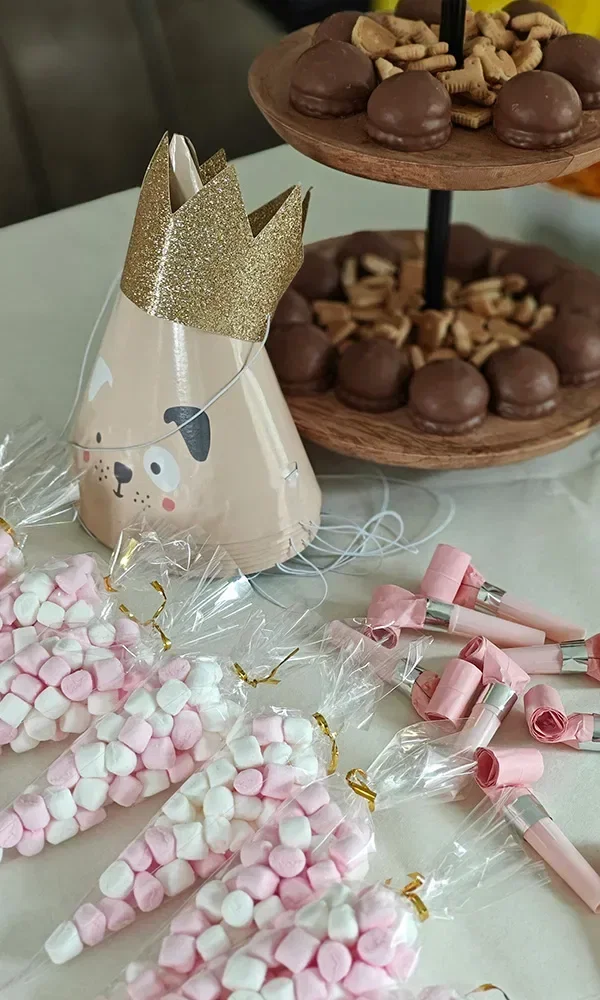 Süßigkeitentüten, gefüllt mit bunten Süßigkeiten und Marshmallows, arrangiert auf einem Tisch neben einem goldglitzernden Kronenhut und einem Plätzchenständer.