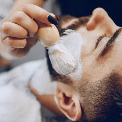 Mann erhält eine luxuriöse Gesichtsbehandlung mit einem Pinsel, der eine Gesichtsmaske aufträgt. Der Mann liegt ruhig und entspannt in einem Spa-Setting.