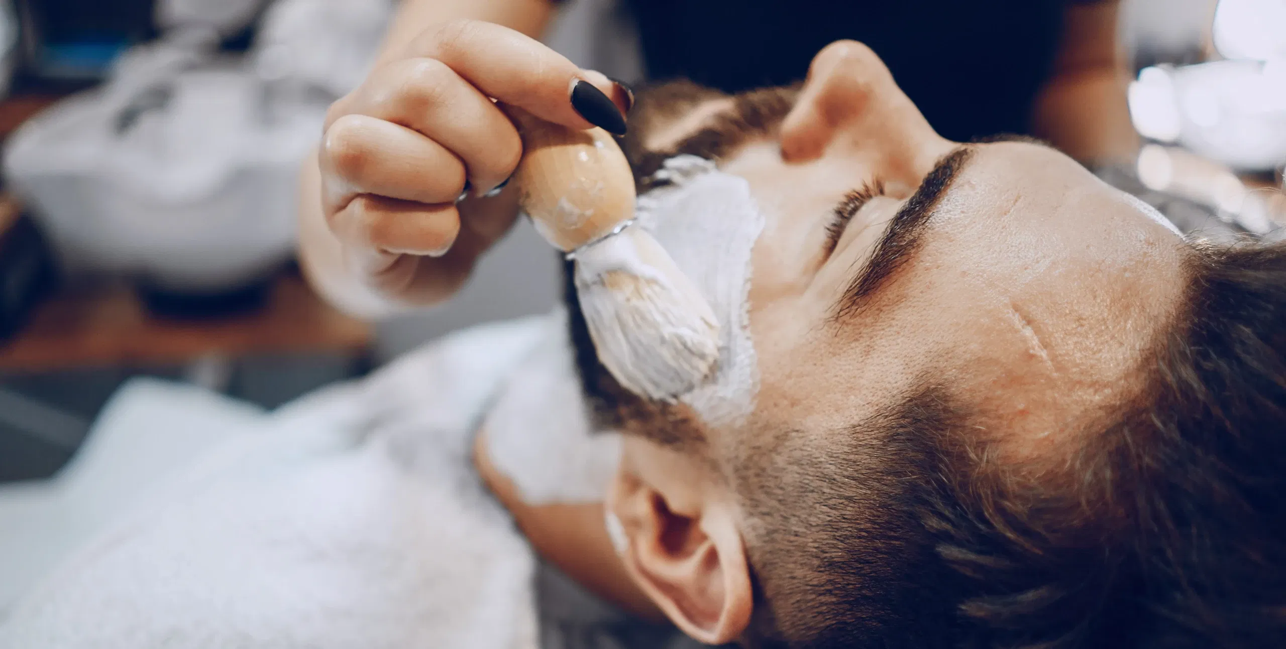 Mann erhält eine luxuriöse Gesichtsbehandlung mit einem Pinsel, der eine Gesichtsmaske aufträgt. Der Mann liegt ruhig und entspannt in einem Spa-Setting.