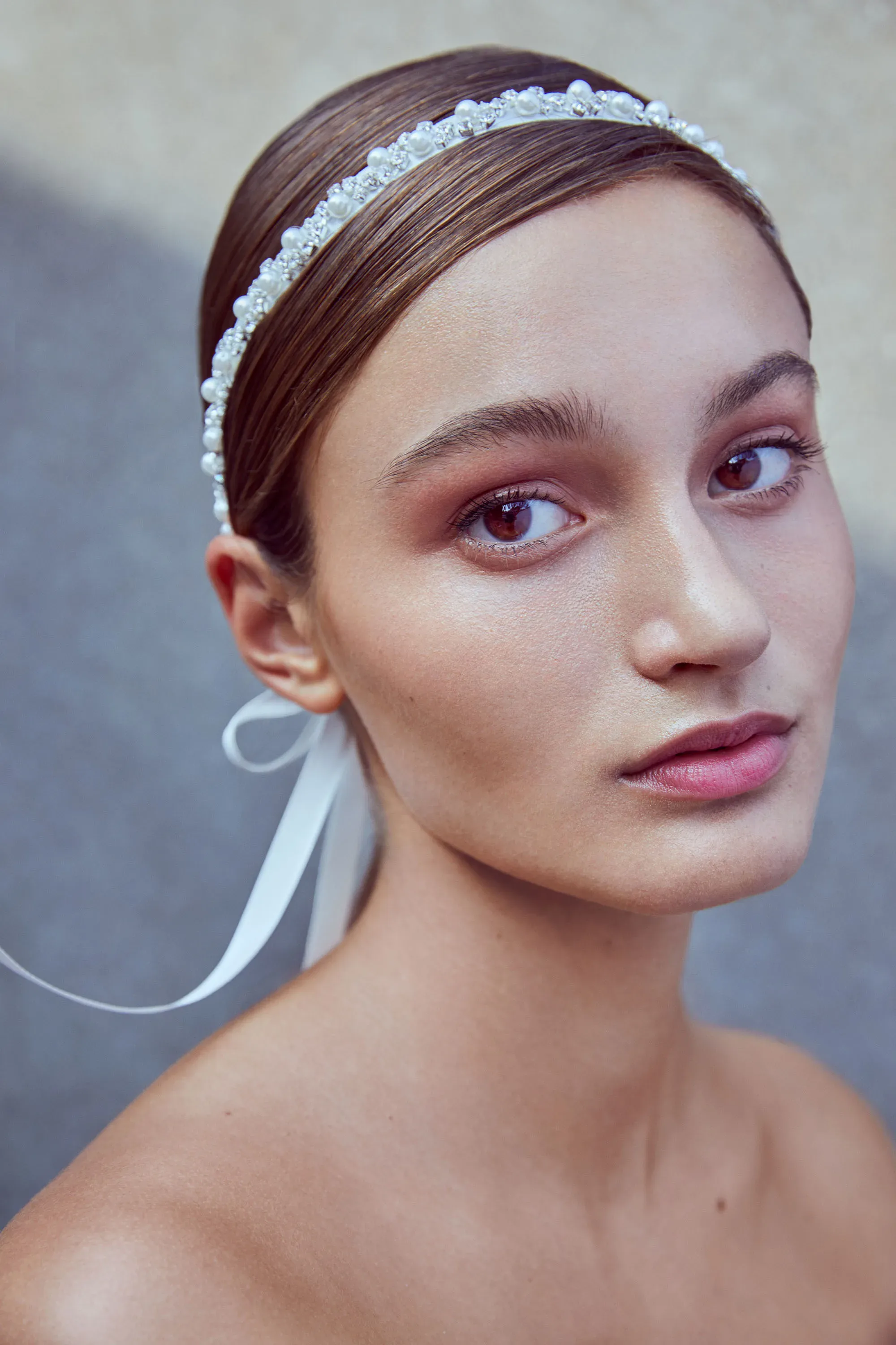 Nahaufnahme einer Braut mit natürlichem Make-up und dezentem, elegantem Stirnband aus Perlen und Schmucksteinen. Ihre Haare sind glatt zurückgebunden.