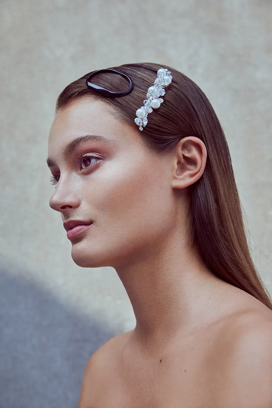 Seitenansicht einer Frau mit geradem, glattem Haar und einer Schmuck-Haarspange. Ihr Make-up ist zart gehalten und betont ihren natürlichen Look.