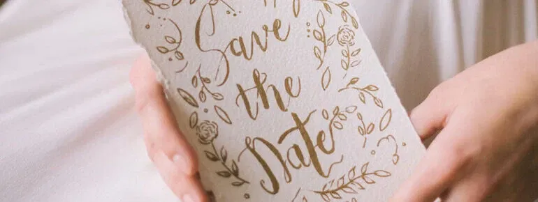 Save-the-Date-Karte in natürlichen Tönen mit verspieltem floralen Design und handgeschriebener Schrift, in der Hand gehalten.