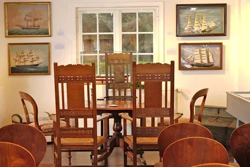 Kleiner, gemütlicher Raum im Sylt-Museum, eingerichtet mit antiken Holzstühlen und maritimen Gemälden an den Wänden. Ein perfekter Ort für eine intime Trauung im Seefahrtsambiente.