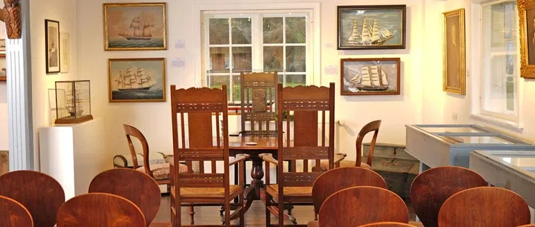 Kleiner, gemütlicher Raum im Sylt-Museum, eingerichtet mit antiken Holzstühlen und maritimen Gemälden an den Wänden. Ein perfekter Ort für eine intime Trauung im Seefahrtsambiente.