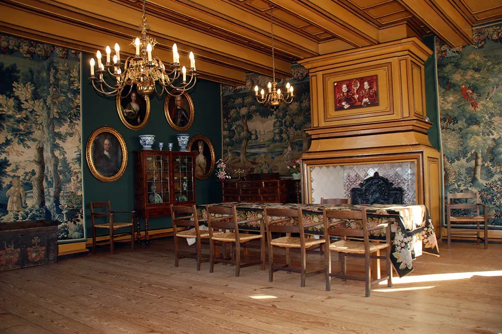 Historischer Ahnensaal mit prächtigen Wandteppichen, klassischen Holzstühlen und einem langen Esstisch. Kronleuchter und Porträts an den Wänden betonen die edle, traditionelle Atmosphäre des Raumes.