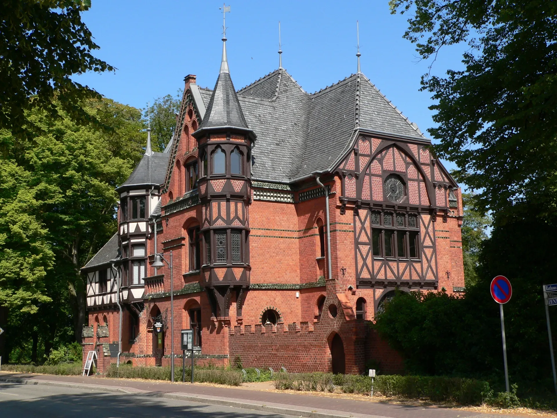 Historisches rotes Backsteingebäude mit Türmen, bekannt als Moeckelhaus, umgeben von Bäumen.