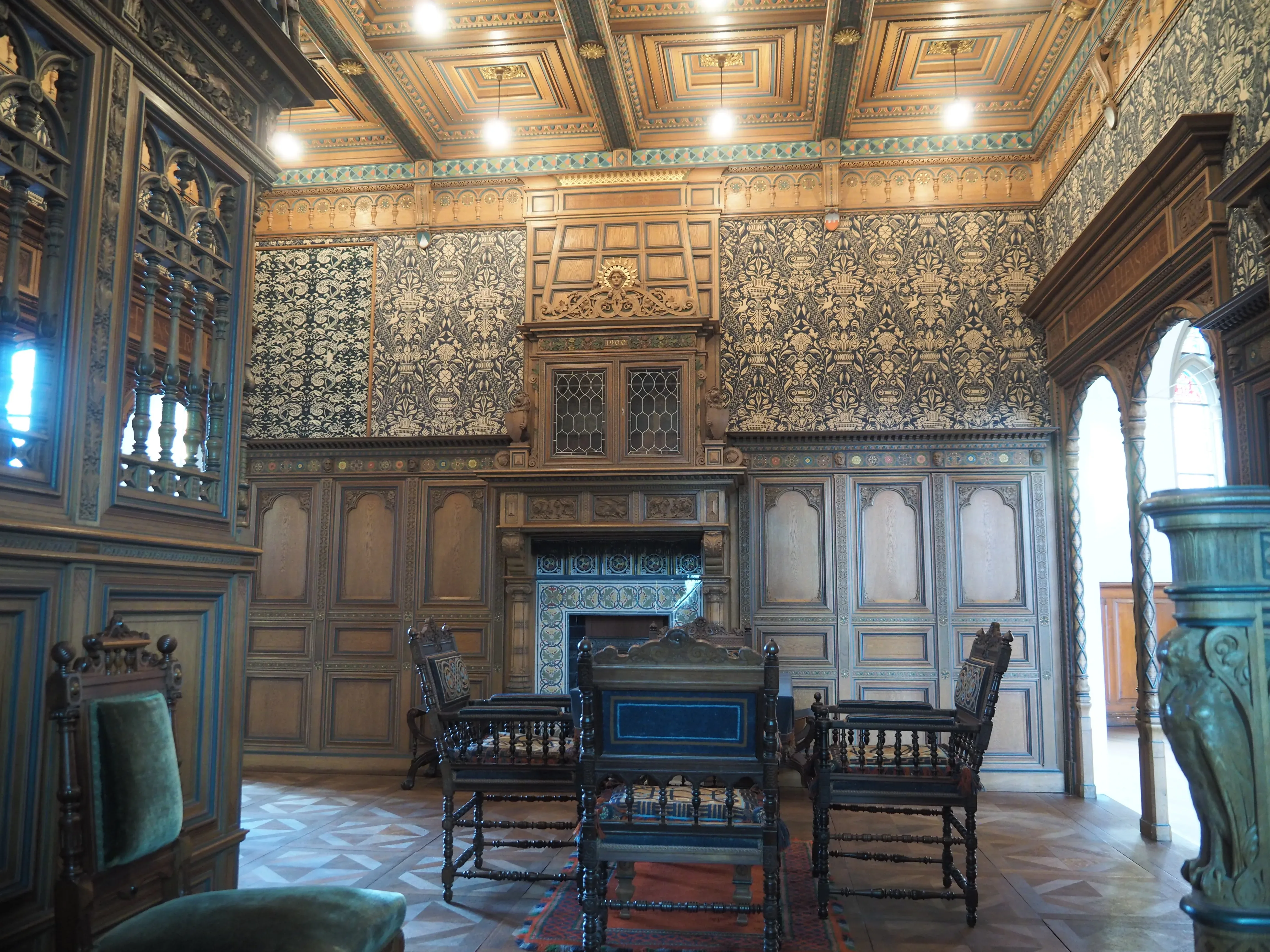 Ein prunkvoller historischer Raum in einem Schloss mit kunstvoller Holzverkleidung und aufwendigen Wandmustern. Antike Möbel und ein aufwändig dekorierter Kamin zieren den Raum.