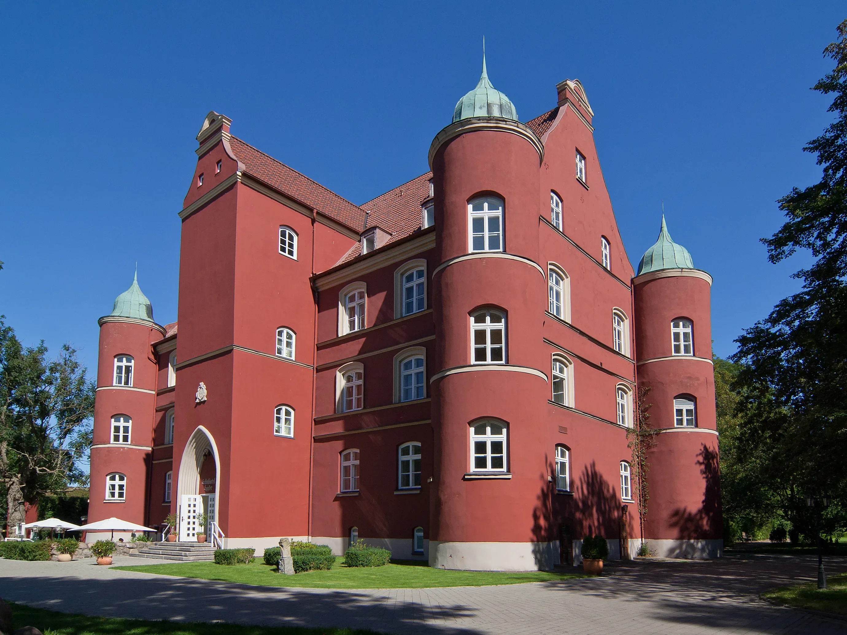 Majestätisches rotes Schloss mit runden Türmen und klarer blauer Himmel im Hintergrund.