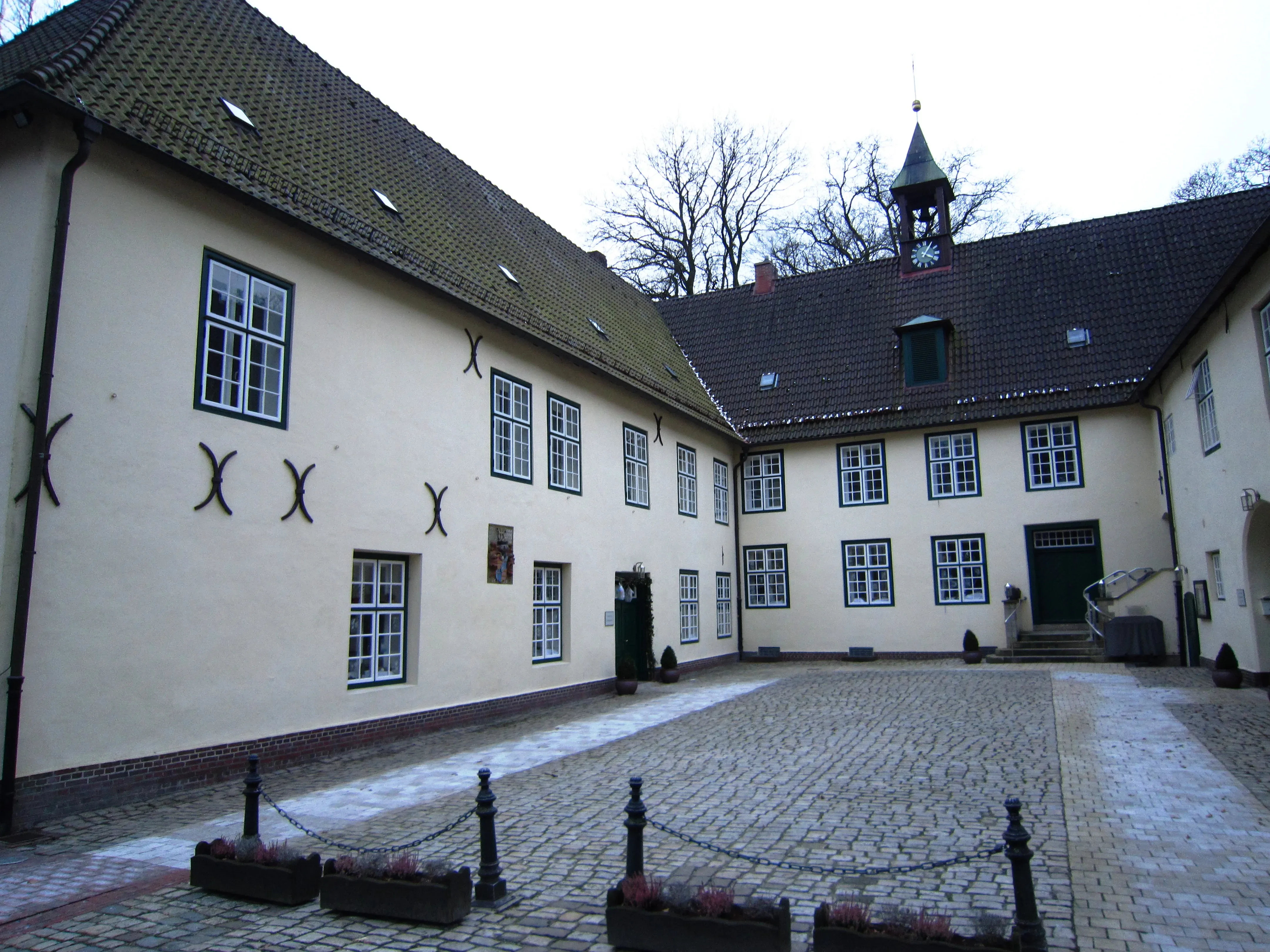 Ein gepflasterter Innenhof eines historischen Schlosses mit hellen Fassaden und einem dunklen Dach. Der Hof ist leer, und ein kleiner Glockenturm ragt über dem Dach hervor.
