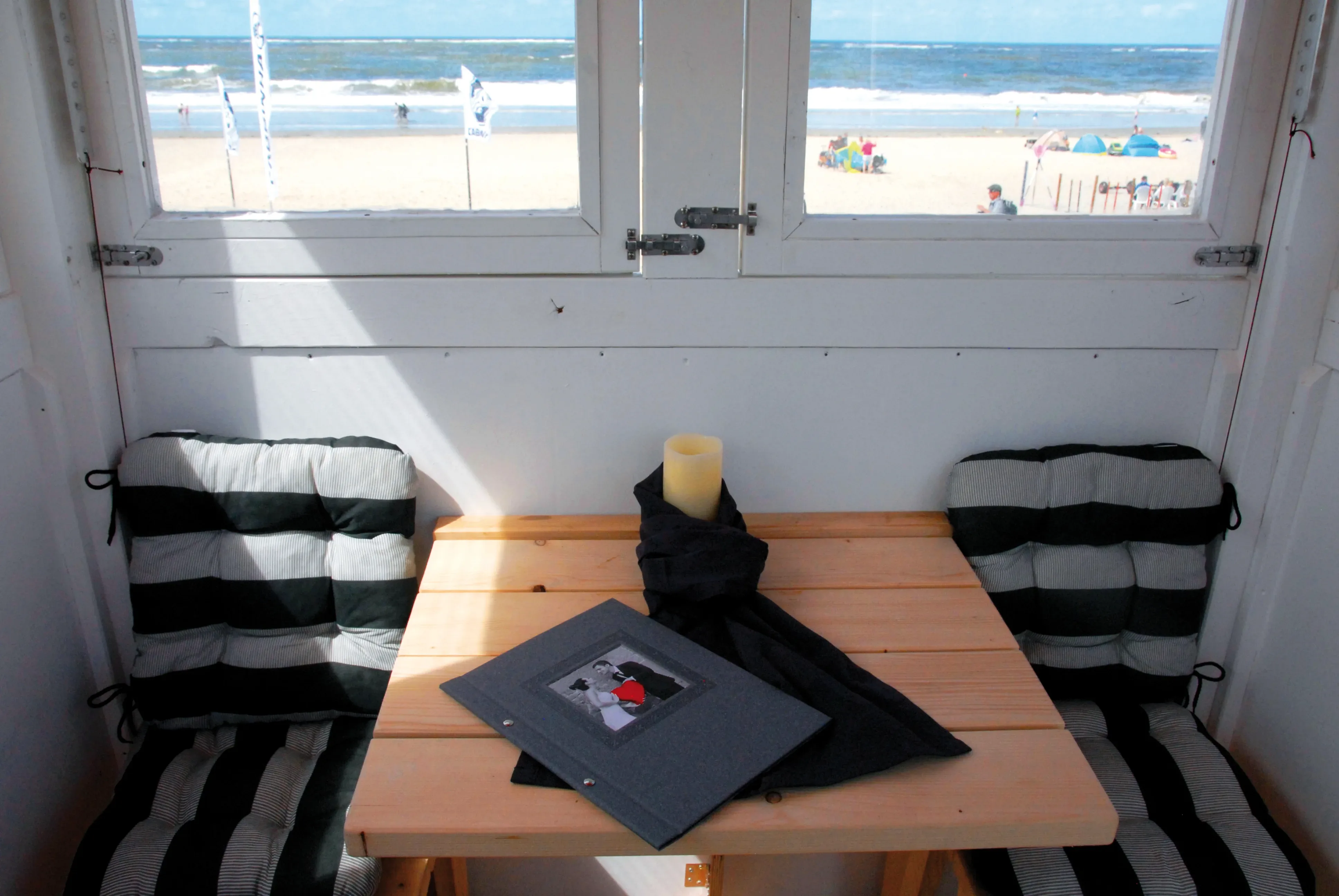 Blick aus einem kleinen Raum am Strand mit gepolsterten Sitzbänken und einem Tisch, der zum Meer hin ausgerichtet ist.