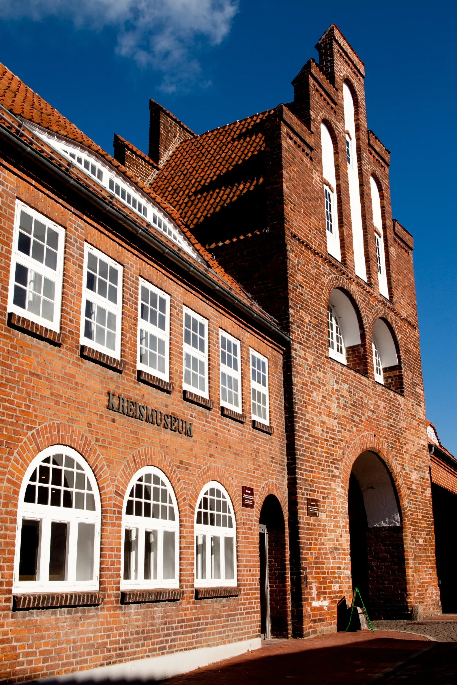 Historische Backsteinfassade des Kreismuseums mit weiß gerahmten Fenstern und einem markanten Bogenportal unter strahlend blauem Himmel.