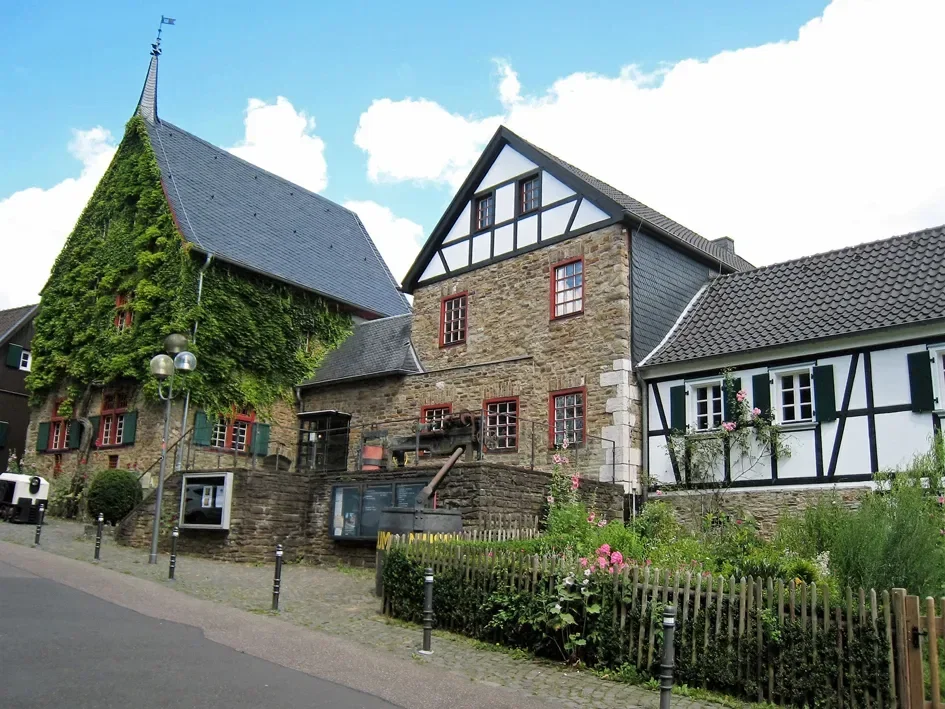 Historische Fachwerkhäuser aus Stein und Holz, liebevoll restauriert, mit grünem Bewuchs und einem malerischen Hof.