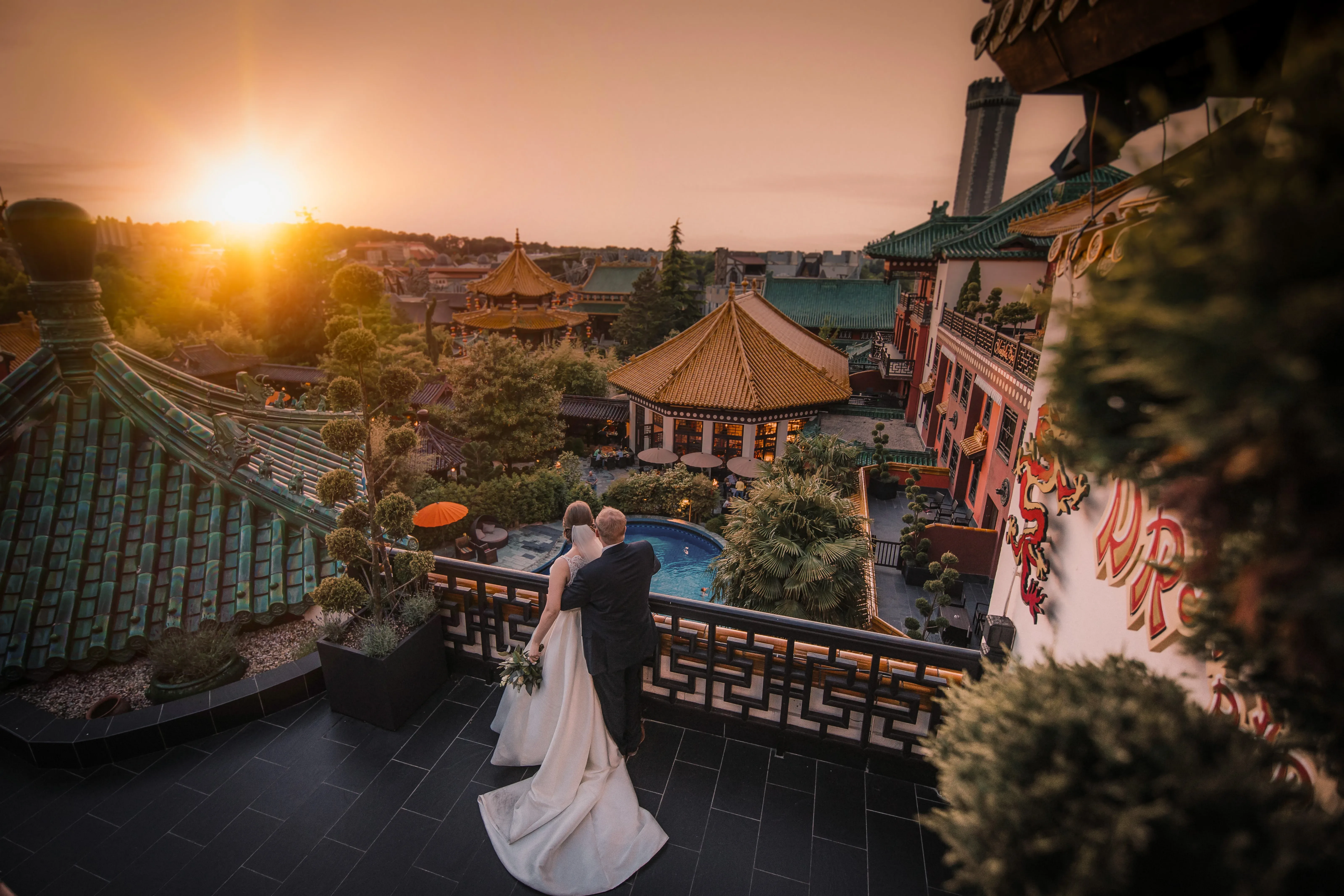 Paar im Phantasialand bei Sonnenuntergang, umgeben von exotischer, asiatisch inspirierter Architektur und üppiger Vegetation.