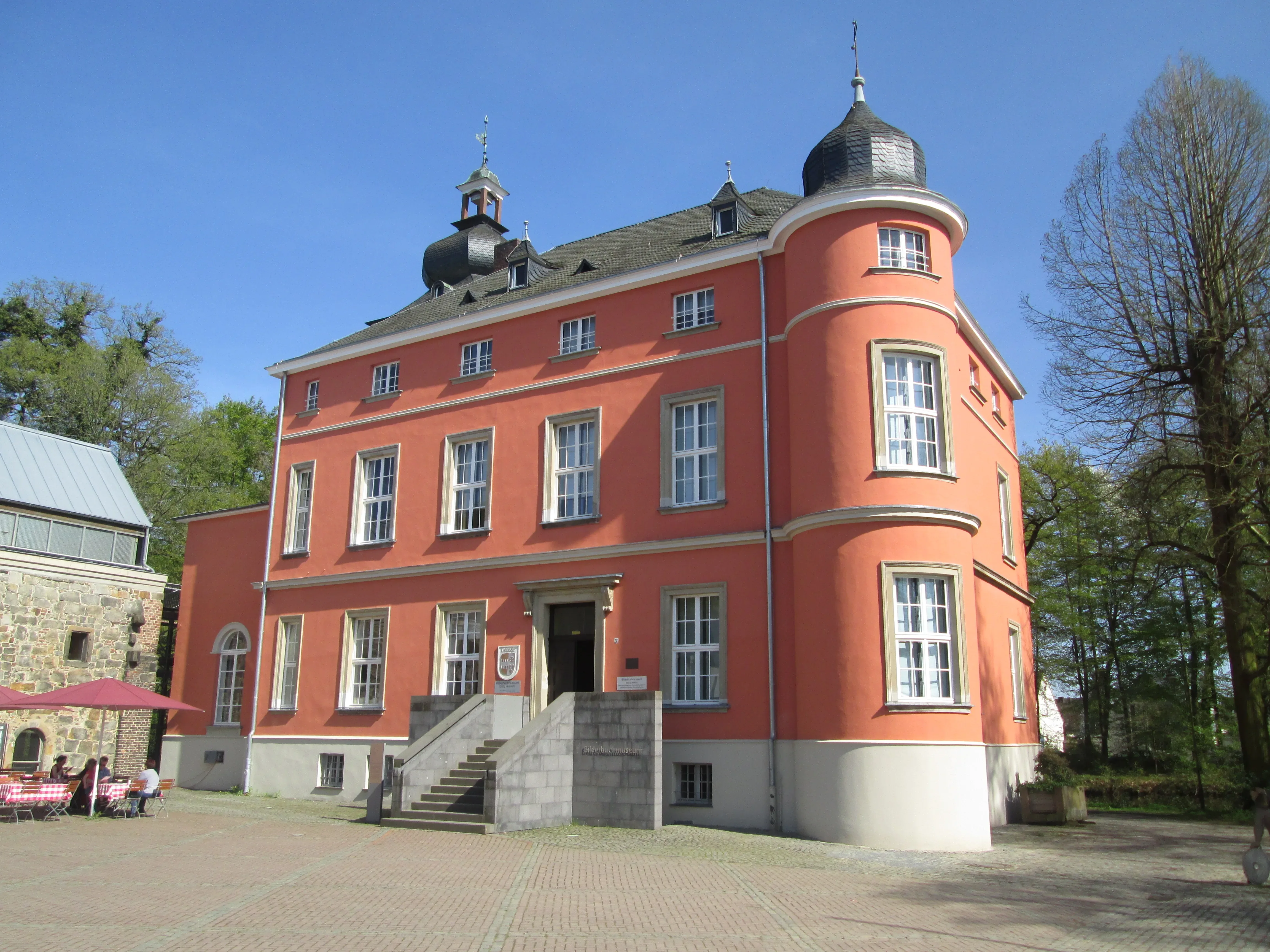 Außenansicht der roten Burg Wissem mit ihrem imposanten Turm bei strahlendem Sonnenschein.