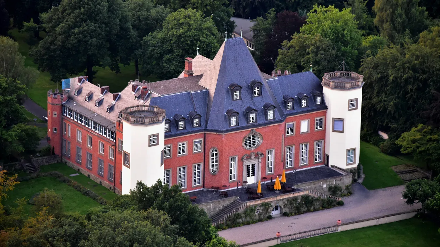 Luftaufnahme von Schloss Birlinghoven, umgeben von Bäumen und grünem Parkgelände.