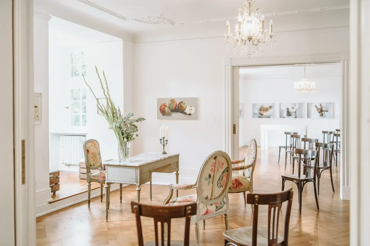 Ein elegant eingerichtetes Zimmer mit floralen Stühlen und einem antiken Schreibtisch, dekoriert mit einer hohen Blumenvase.