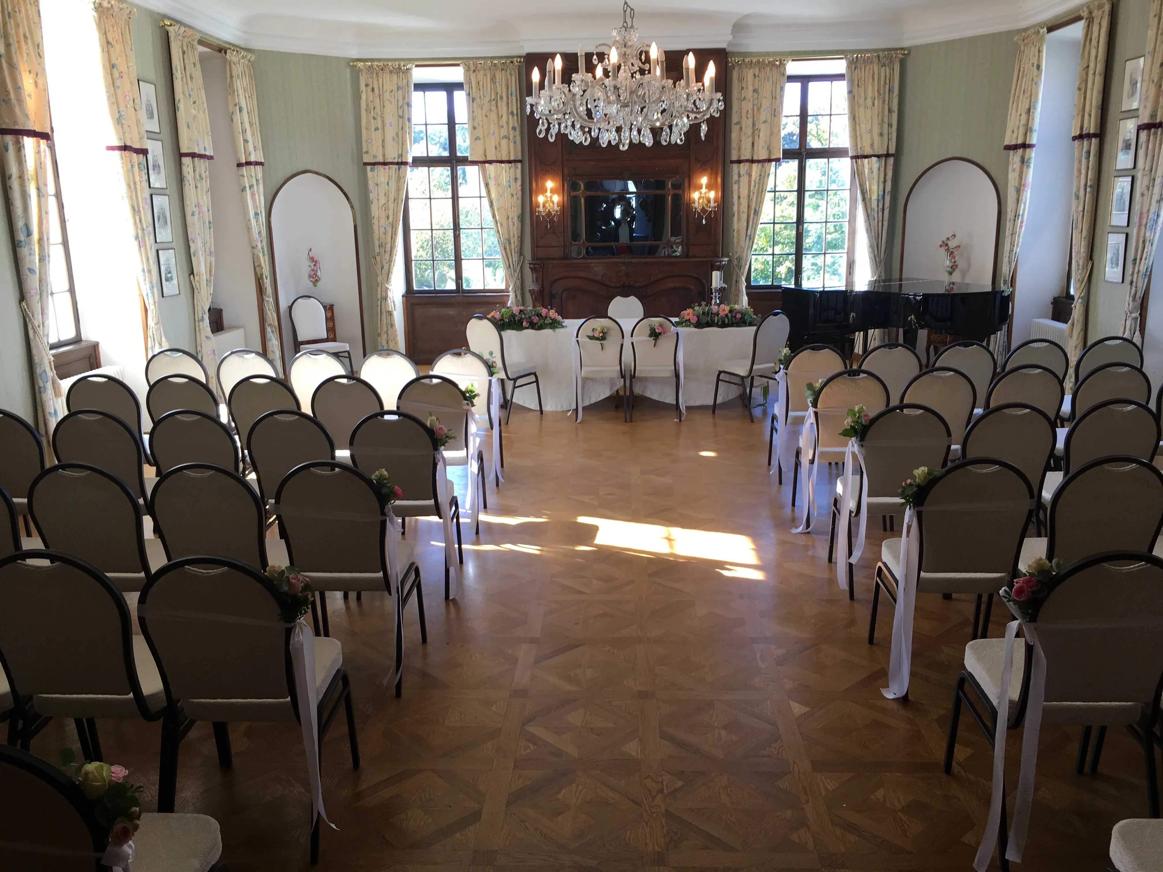 Historischer Festsaal mit weißen Stühlen und einem dekorierten Tisch, ideal für intime Hochzeitszeremonien.