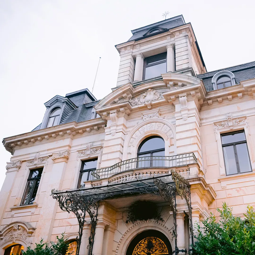 Detailansicht der prächtigen Fassade der Villa Stella Rheni in Bonn, einem historischen Gebäude mit kunstvollen Verzierungen, großen Fenstern und einem dekorativen Balkongeländer unter hellem Himmel.