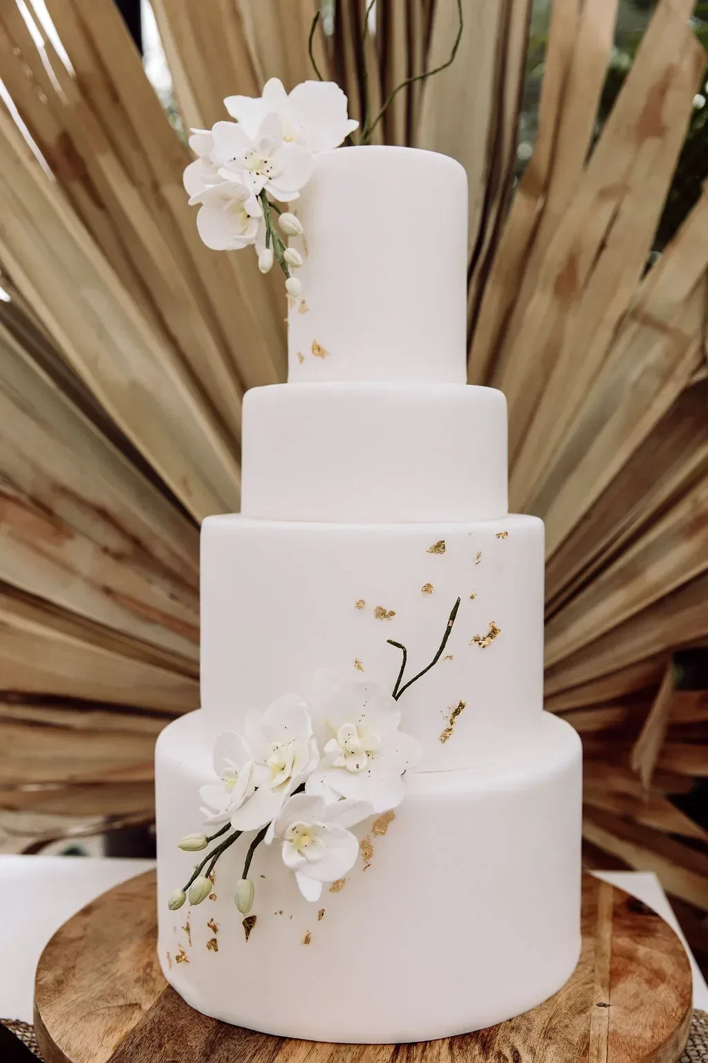 Elegante, dreistöckige weiße Hochzeitstorte mit Orchideen und goldenen Details, inspiriert vom tropischen Bali-Stil