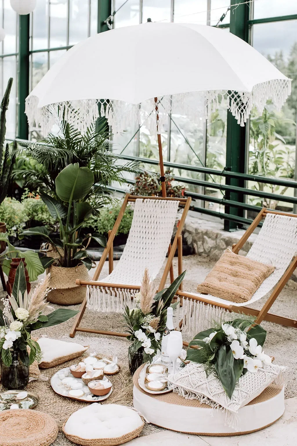 Gemütliche Lounge-Ecke mit Makramee-Stühlen, tropischen Pflanzen und einem weißen Sonnenschirm, dekoriert für eine Bali-inspirierte Hochzeit.