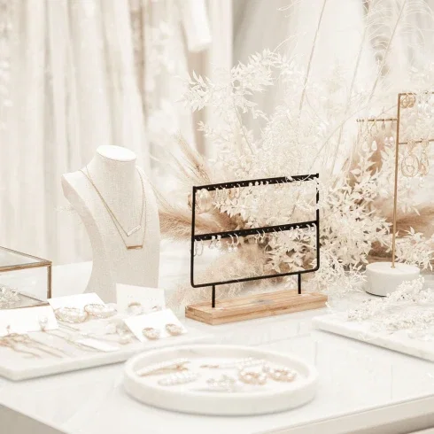 Detailaufnahme von Schmuck und Accessoires in einem modernen Bridal-Shop, elegant arrangiert auf einem weißen Tisch mit floraler Dekoration.