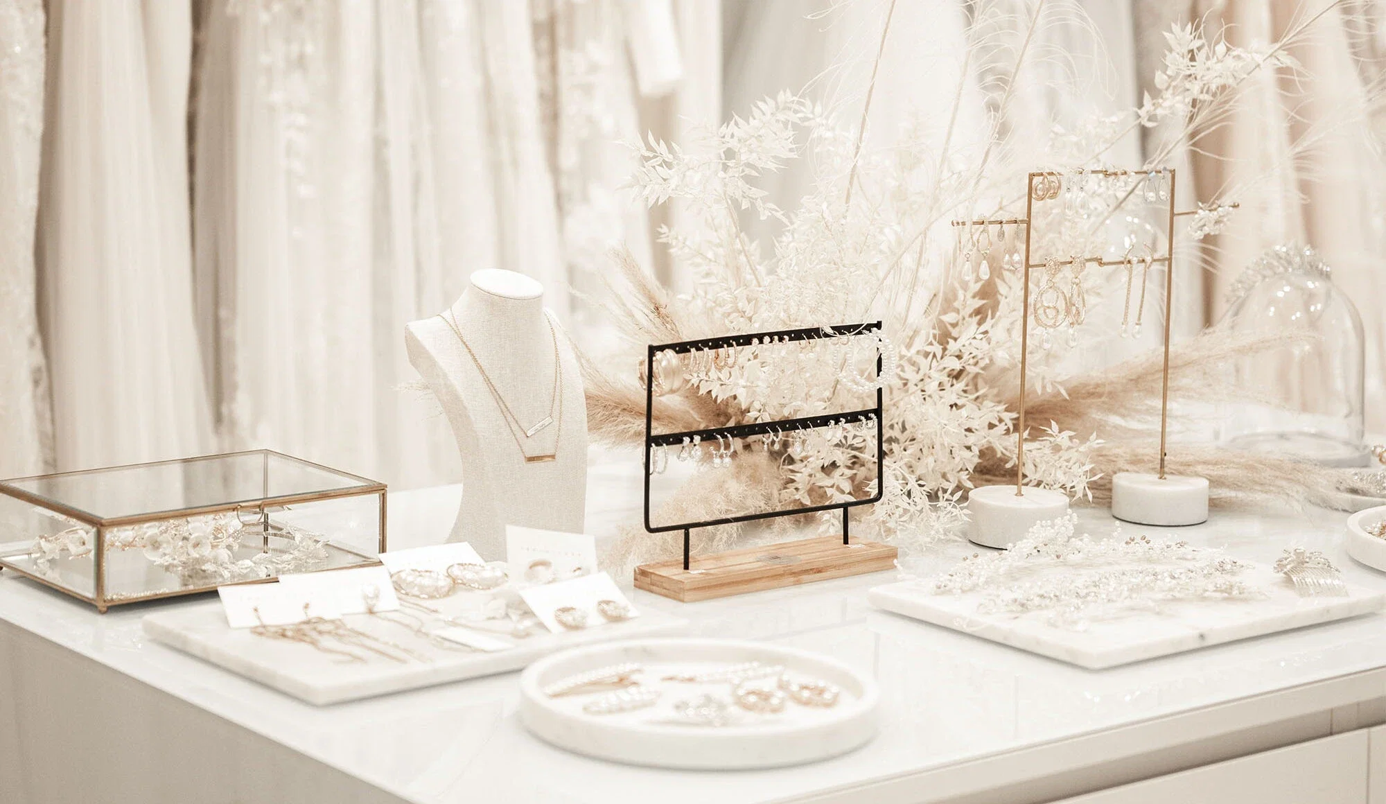 Detailaufnahme von Schmuck und Accessoires in einem modernen Bridal-Shop, elegant arrangiert auf einem weißen Tisch mit floraler Dekoration.