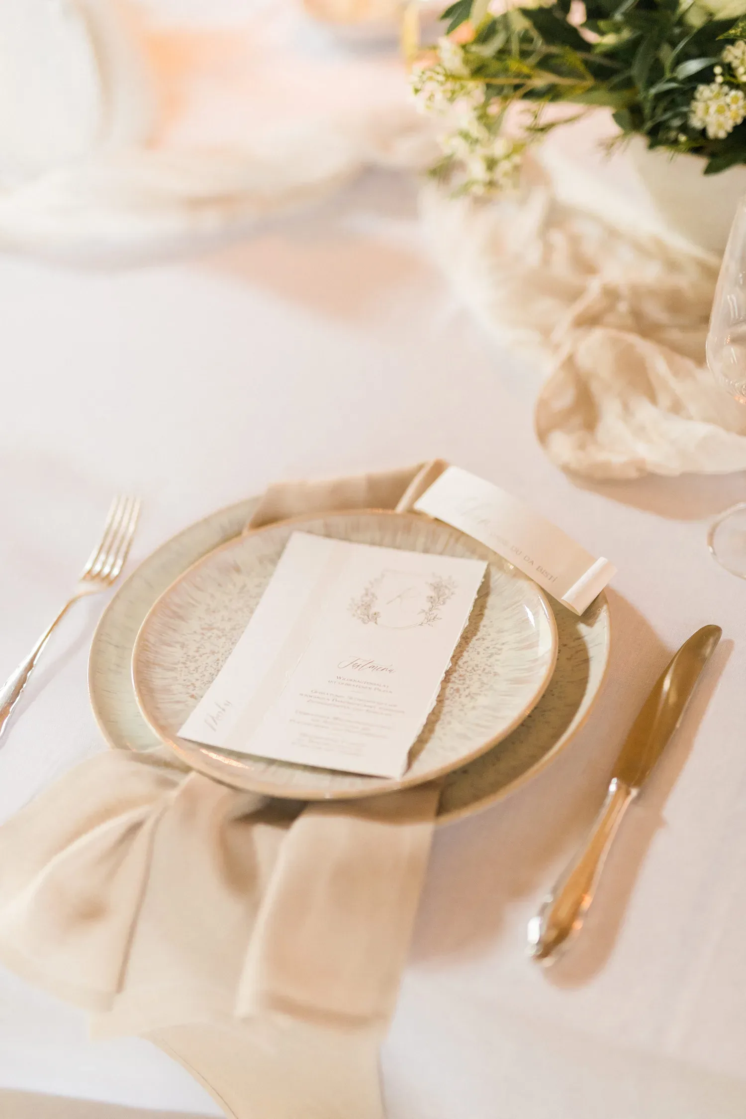 Nahaufnahme eines eleganten Hochzeitstischs mit cremefarbenem Geschirr und einem dezent gestalteten Menü auf dem Teller.