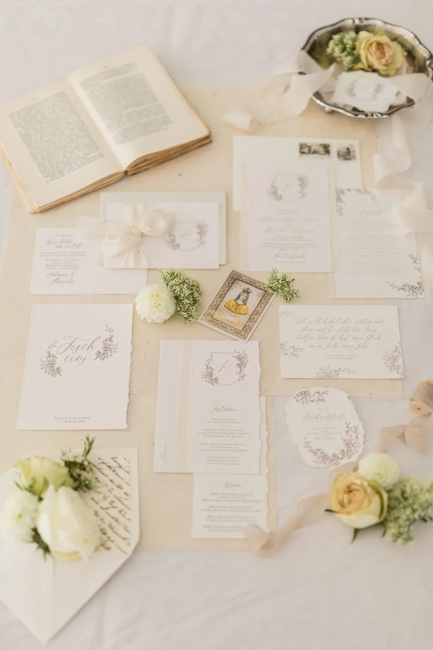 Elegante Hochzeitseinladung in Weiß- und Cremetönen, kunstvoll arrangiert mit weißen Blüten und einer Vintage-Silberschale.